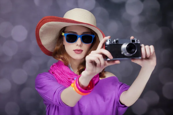 Divertente rossa ragazza in cappello con fotocamera e bokeh sullo sfondo — Foto Stock