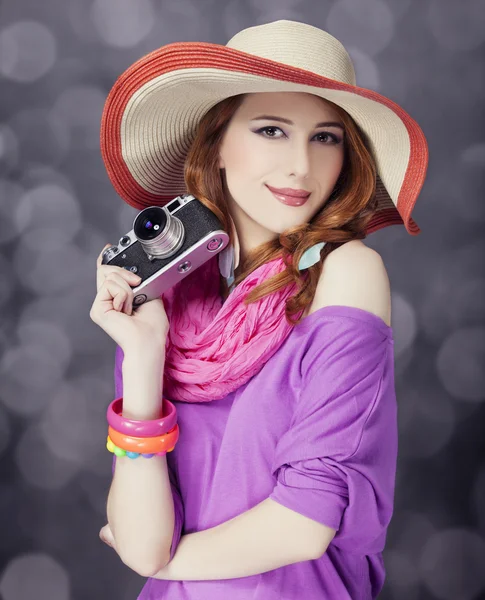 Αστεία κοκκινομάλλα κοπέλα με καπέλο με κάμερα και bokeh στο παρασκήνιο — Φωτογραφία Αρχείου