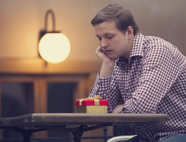 Sad man sittting in cafe with gift — Stock Photo, Image