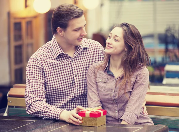 El joven le da un regalo a una joven en el café y ellos — Foto de Stock