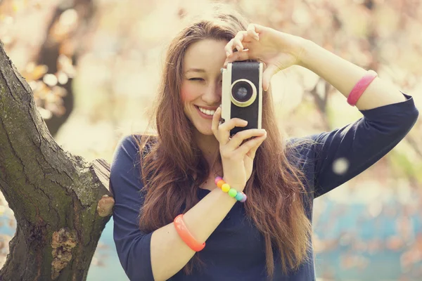 Девушка в очках с винтажной камерой рядом с цветущим деревом — стоковое фото