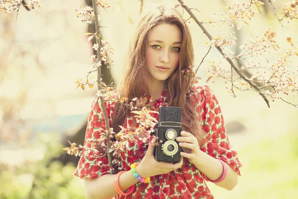 Dziewczyna w okularach z rocznika kamery w pobliżu kwitnąć drzewa — Zdjęcie stockowe