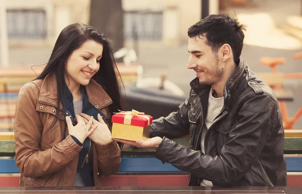 The young man gives a gift to a young girl in the cafe and they — Stock Photo, Image