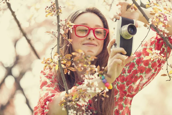 Chica adolescente en gafas con cámara vintage cerca de árbol de flores —  Fotos de Stock