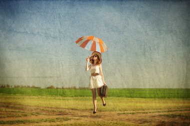 Redhead enchantress with umbrella and suitcase at spring country