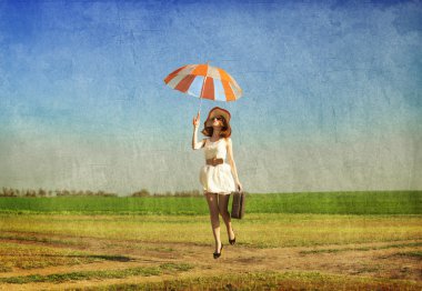 Redhead enchantress with umbrella and suitcase at spring country