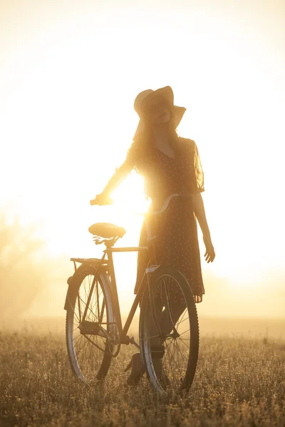 Chica en una bicicleta en el campo en el amanecer — Foto de Stock