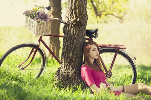 Beautiful girl sitting near bike and tree at rest in forest. Pho