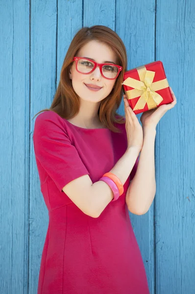 Rossa ragazza in occhiali con regalo vicino fondo di legno — Foto Stock