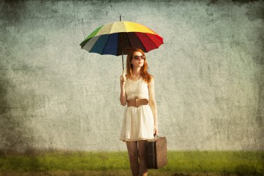 Redhead enchantress with umbrella and suitcase at spring country