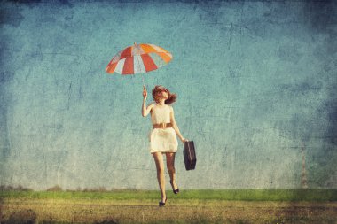Redhead enchantress with umbrella and suitcase at spring country