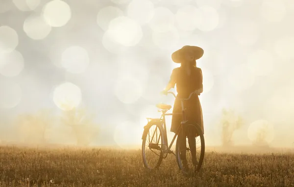 Chica y en una bicicleta en el campo en el amanecer — Foto de Stock