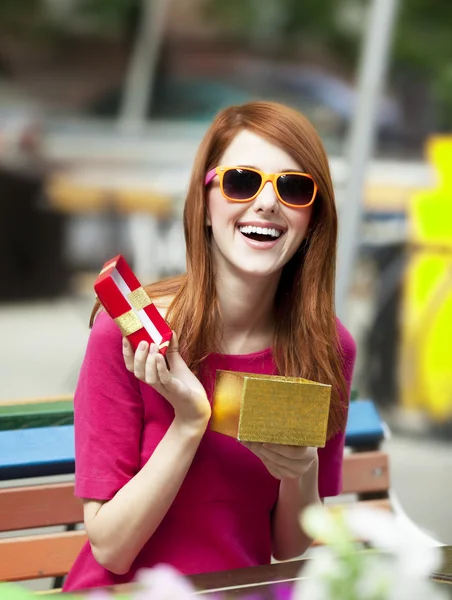 Estilo chica pelirroja con regalo sentado en el banco en la cafetería — Foto de Stock