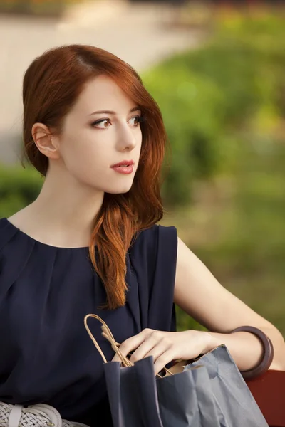 Style redhead women sitting on the bench with shopping bags — Stock Photo, Image