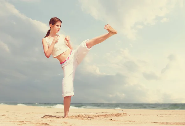 Mujer atlética realizando una patada en una playa de arena — Foto de Stock