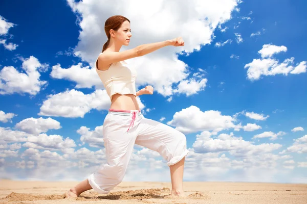 Femme sportive effectuant un coup de pied dans une plage de sable — Photo