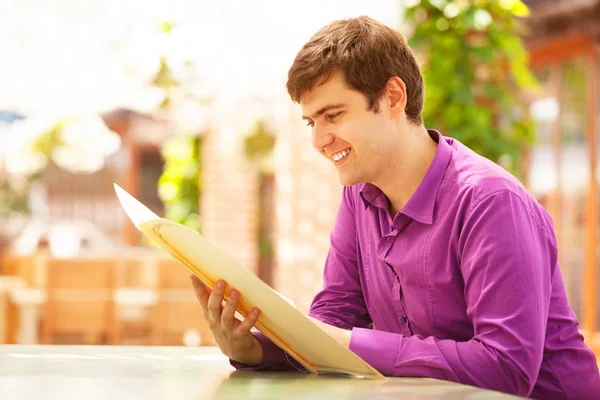 Jeune homme assis dans le café et regardant dans le menu . — Photo