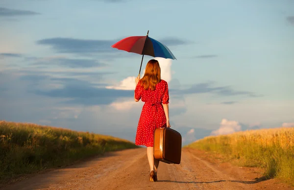 Ragazza rossa con ombrello e valigia all'aperto — Foto Stock