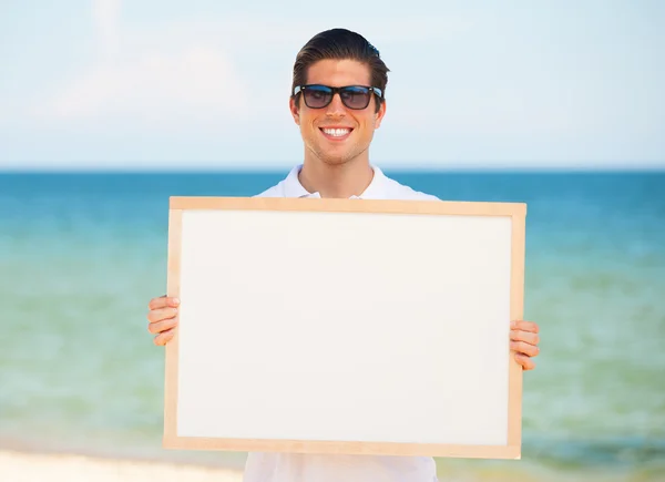 Bello giovane uomo con lavagna su sfondo spiaggia — Foto Stock