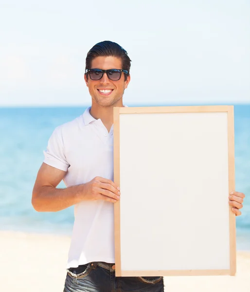Przystojny młody mężczyzna z tablica na tle plaży — Zdjęcie stockowe