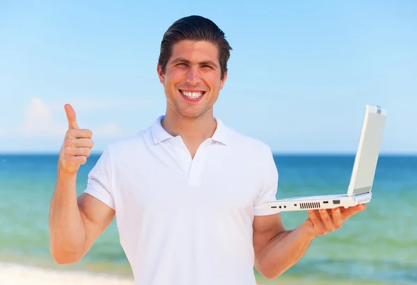 Jovem bonito com laptop no fundo da praia — Fotografia de Stock