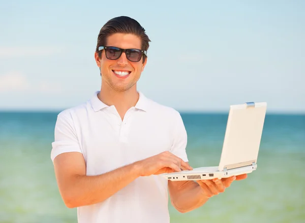 Όμορφος νεαρός άνδρας με το laptop στην παραλία φόντο — Φωτογραφία Αρχείου