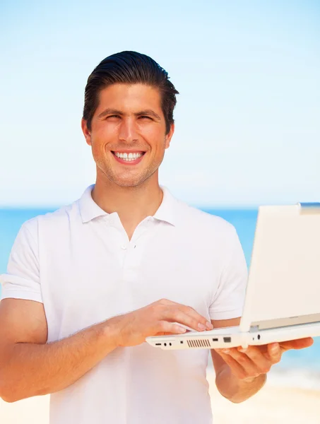 Bello giovane uomo con computer portatile in spiaggia sfondo — Foto Stock