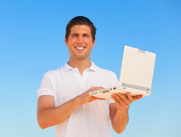 Stilig ung man med laptop på blå himmel bakgrund — Stockfoto