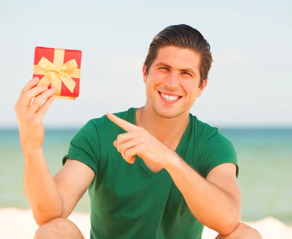 Jovem bonito com presente no fundo da praia — Fotografia de Stock