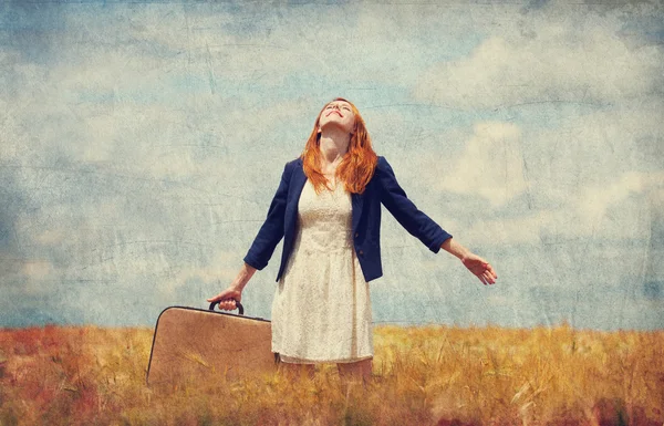 Redhead girl with suitcase at spring wheat field. — Stock Photo, Image