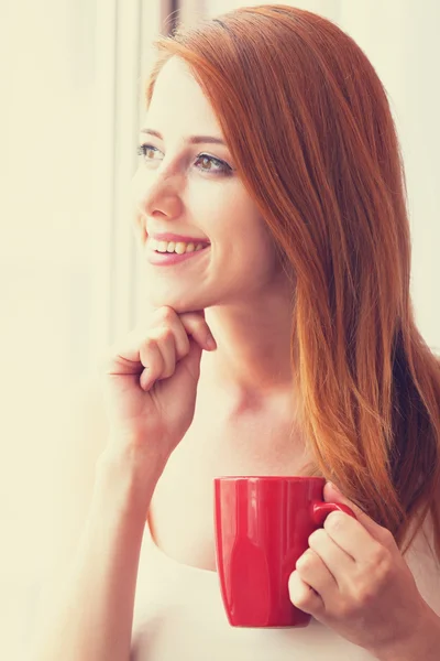 Beautiful young woman with cup over window. — Stock Photo, Image