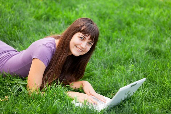 Morena chica en verde hierba con portátil — Foto de Stock