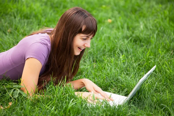 ノートブックで緑の草にブルネットの少女 — ストック写真