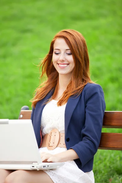 Ruiva menina sentada no banco com notebook — Fotografia de Stock