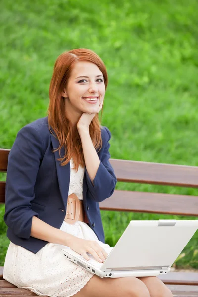 Redhead girl sitting at the bench with notebook — Stock Photo, Image