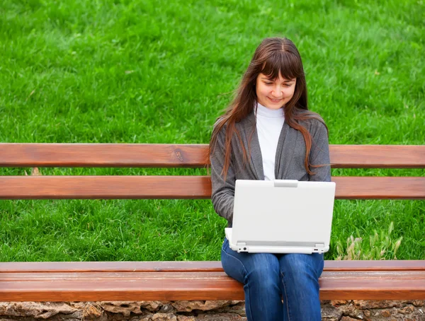Morena menina sentada no banco com notebook — Fotografia de Stock