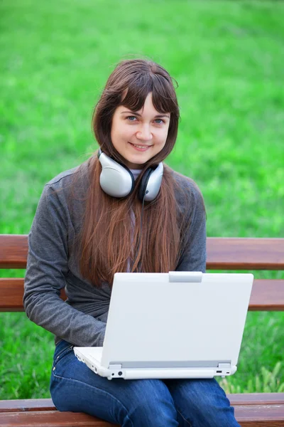 Morena menina sentada no banco com notebook — Fotografia de Stock