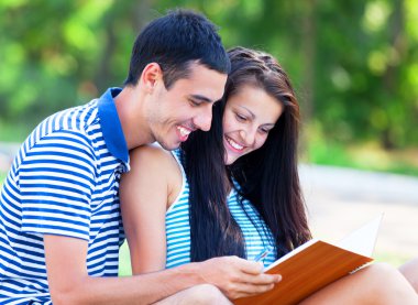 Not Defteri ile yeşil çimenlerin üzerinde oturan genç öğrenciler.