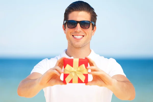 Schöner junger Mann mit Geschenk am Strand — Stockfoto
