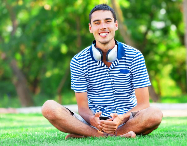 Beau jeune homme avec écouteurs à l'herbe verte — Photo