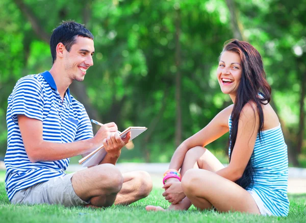 Jonge studenten zittend op groen gras met Opmerking boek. — Stockfoto