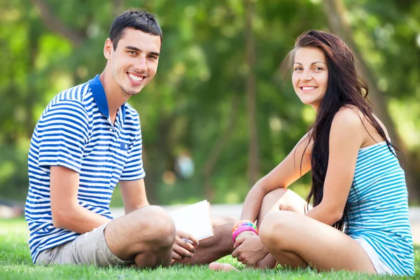 Młodzi uczniowie siedzący na zielonej trawie z książki pamiętać. — Zdjęcie stockowe