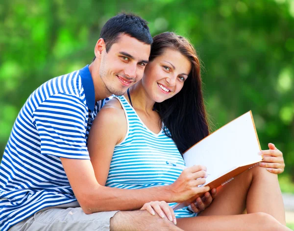 Jonge studenten zittend op groen gras met Opmerking boek. — Stockfoto