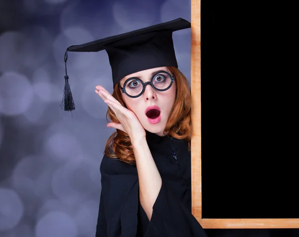 Graduating student girl in an academic gown near blackboard — Stock Photo, Image