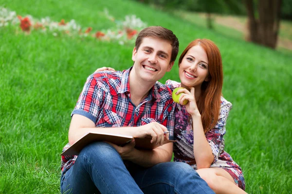 Unga studenter sitter på grönt gräs med anteckningsbok. — Stockfoto