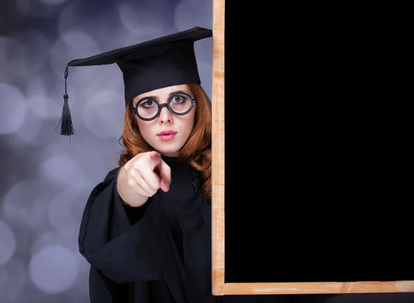 Kara tahtanın yanında akademik bir elbiseyle mezun olan kız. — Stok fotoğraf