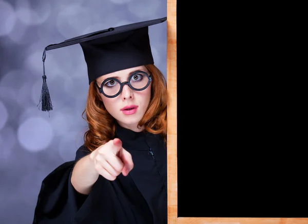 Kara tahtanın yanında akademik bir elbiseyle mezun olan kız. — Stok fotoğraf