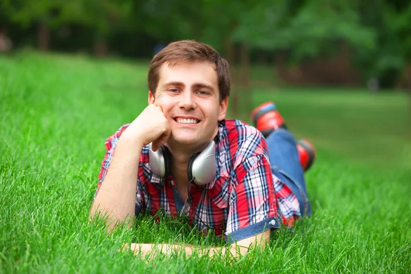 Knappe jonge man met hoofdtelefoon op groen gras — Stockfoto