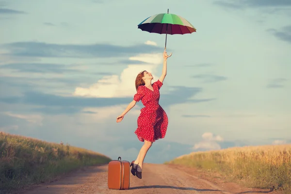 Ragazza rossa con ombrello e valigia all'aperto — Foto Stock