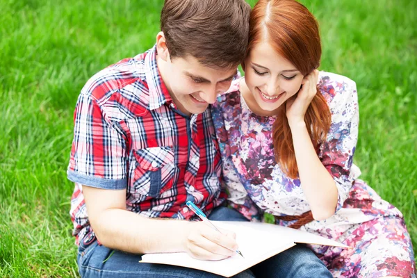 Jóvenes estudiantes sentados sobre hierba verde con cuaderno . — Foto de Stock